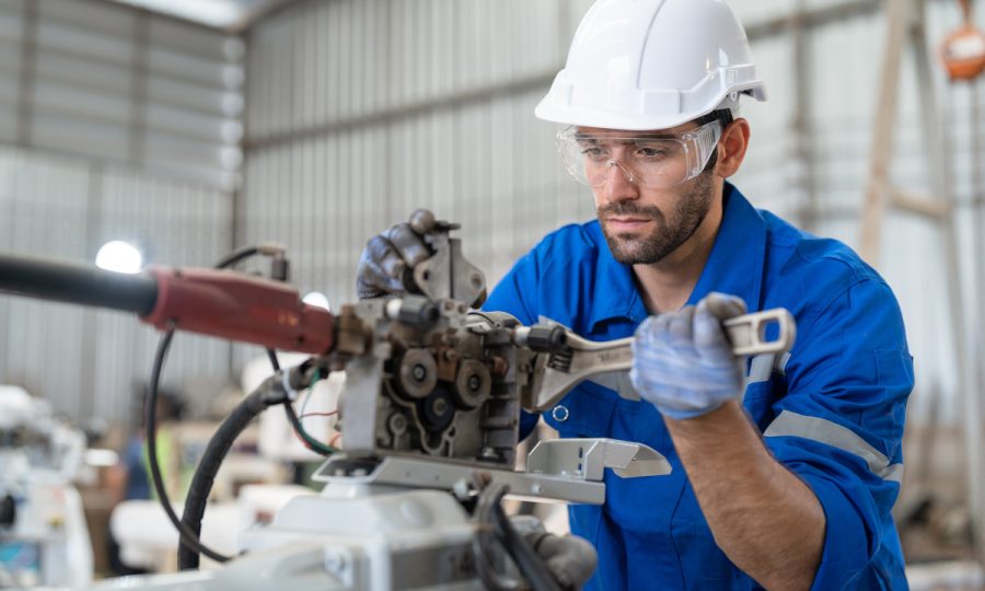 Male engineer using wrench tool repair robot arm welding machine in factory. Technician automation robot in uniform working at robot industrial.