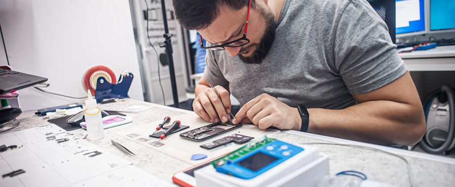 Workplace top view, close-up. In an electronics repair shop, a repairman repairs a smartphone, uses tweezers as one of the many work tools.