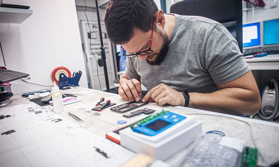 Workplace top view, close-up. In an electronics repair shop, a repairman repairs a smartphone, uses tweezers as one of the many work tools.